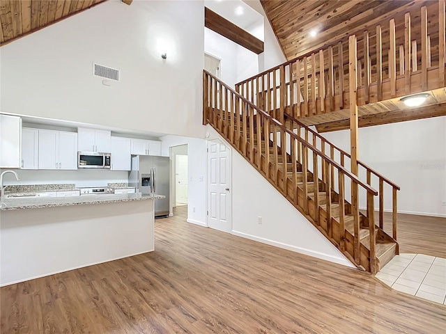 kitchen featuring hardwood / wood-style floors, white cabinetry, stainless steel appliances, and high vaulted ceiling