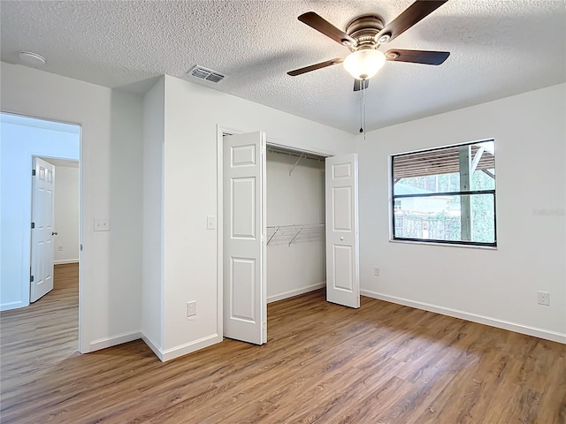 unfurnished bedroom featuring wood-type flooring, a textured ceiling, a closet, and ceiling fan