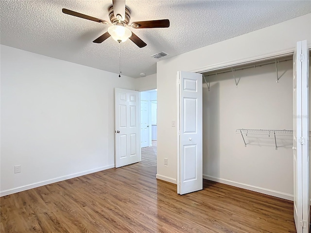 unfurnished bedroom featuring a closet, ceiling fan, hardwood / wood-style floors, and a textured ceiling