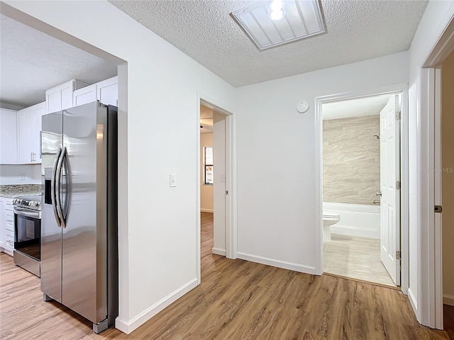 corridor with a textured ceiling and light hardwood / wood-style flooring