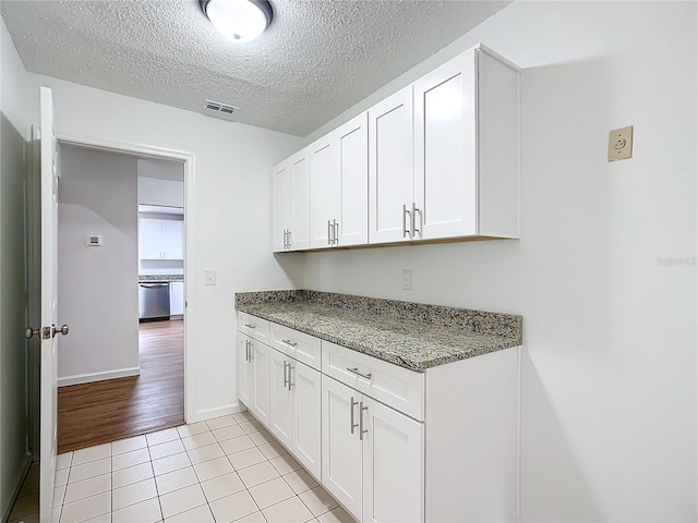 kitchen featuring white cabinets, light tile patterned flooring, stainless steel dishwasher, and dark stone countertops