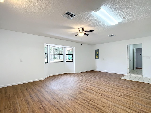 empty room with hardwood / wood-style floors, ceiling fan, a textured ceiling, and electric panel