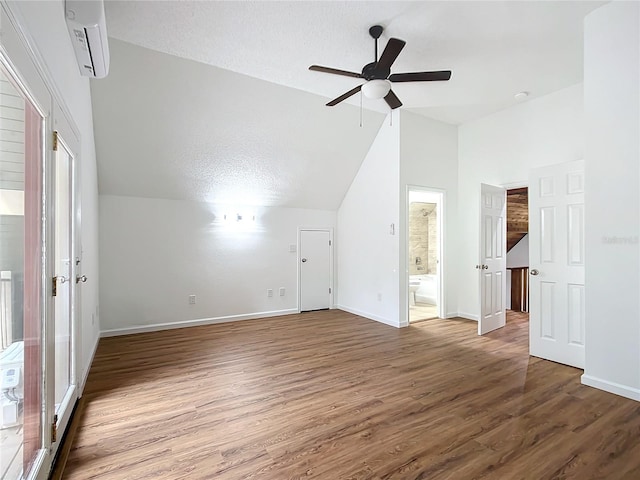 additional living space with a textured ceiling, vaulted ceiling, a wall mounted AC, ceiling fan, and hardwood / wood-style floors