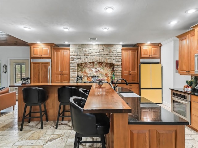 kitchen with a breakfast bar, a large island with sink, built in appliances, and sink