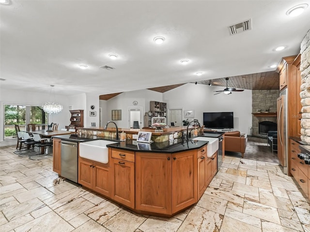 kitchen with a center island with sink, a stone fireplace, sink, and stainless steel appliances