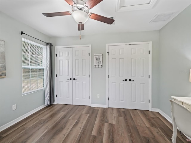 unfurnished bedroom with multiple closets, ceiling fan, and dark wood-type flooring