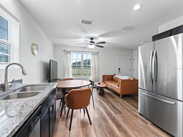 kitchen with light wood-type flooring, light stone counters, stainless steel appliances, ceiling fan, and sink