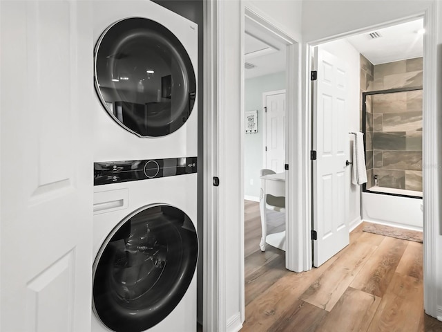 laundry area featuring stacked washing maching and dryer and light hardwood / wood-style flooring