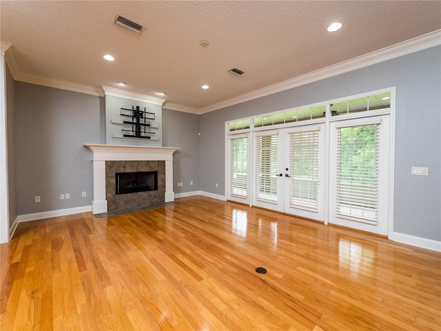 unfurnished living room with ornamental molding, a tiled fireplace, a textured ceiling, and light hardwood / wood-style flooring