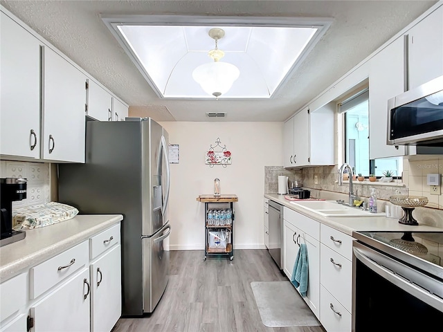 kitchen featuring white cabinetry, sink, stainless steel appliances, backsplash, and decorative light fixtures