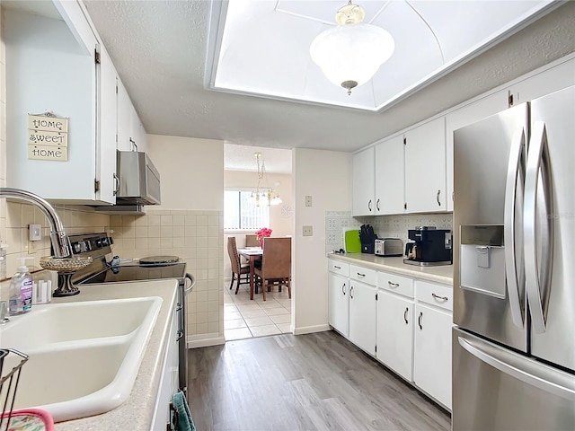 kitchen with white cabinetry, range with electric stovetop, stainless steel fridge, a chandelier, and decorative light fixtures