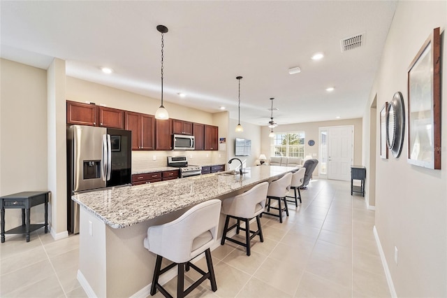 kitchen featuring appliances with stainless steel finishes, ceiling fan, a center island with sink, hanging light fixtures, and a breakfast bar area