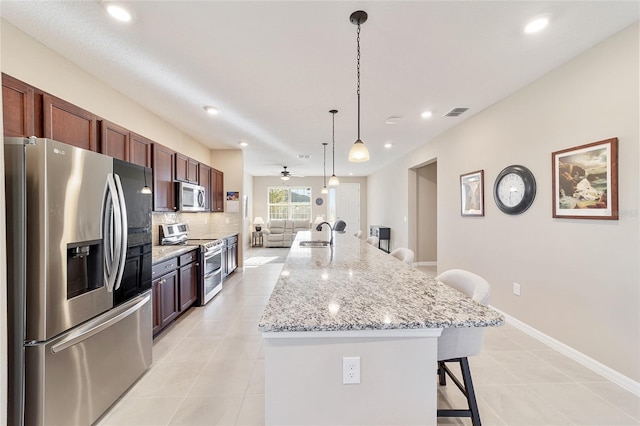 kitchen featuring ceiling fan, a kitchen breakfast bar, pendant lighting, a kitchen island with sink, and appliances with stainless steel finishes