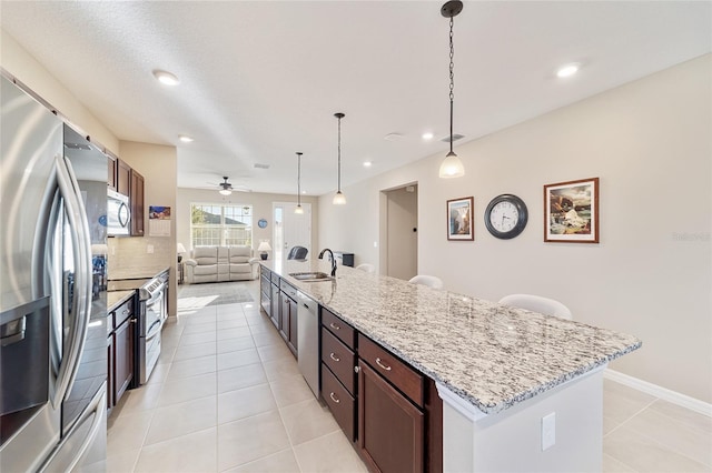 kitchen featuring a kitchen island with sink, sink, hanging light fixtures, light tile patterned flooring, and stainless steel appliances