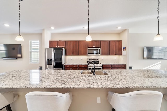 kitchen featuring backsplash, sink, a breakfast bar area, decorative light fixtures, and stainless steel appliances