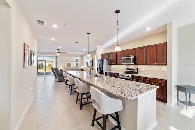 kitchen with a kitchen island with sink, a kitchen breakfast bar, ceiling fan, appliances with stainless steel finishes, and light tile patterned flooring