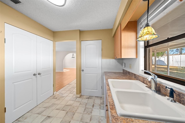 kitchen with pendant lighting, tasteful backsplash, sink, and a textured ceiling