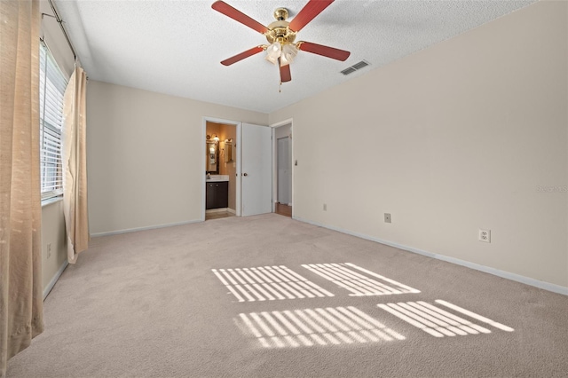 unfurnished bedroom featuring light carpet, a textured ceiling, ensuite bath, and ceiling fan