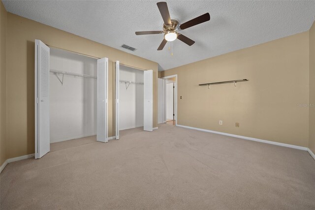 unfurnished bedroom featuring ceiling fan, light colored carpet, a textured ceiling, and multiple closets