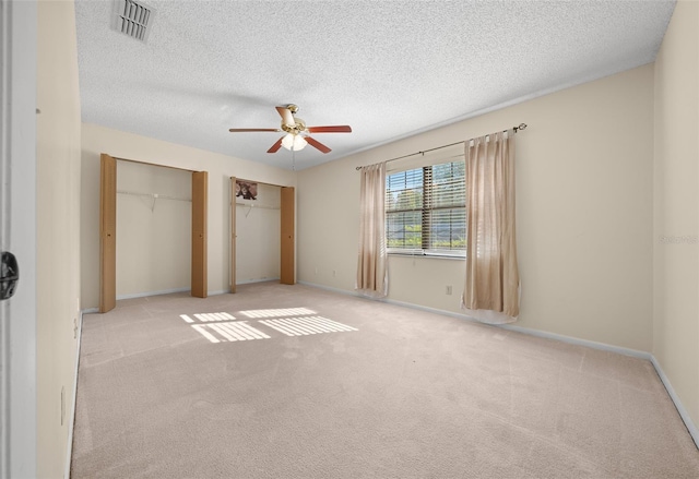 unfurnished bedroom with light carpet, a textured ceiling, two closets, and ceiling fan