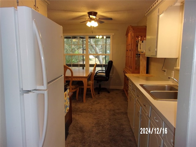 kitchen with dark carpet, sink, ceiling fan, white fridge, and white cabinetry