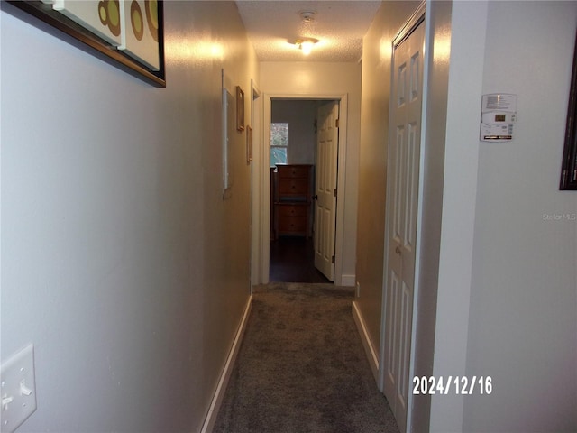 hallway with a textured ceiling and dark carpet