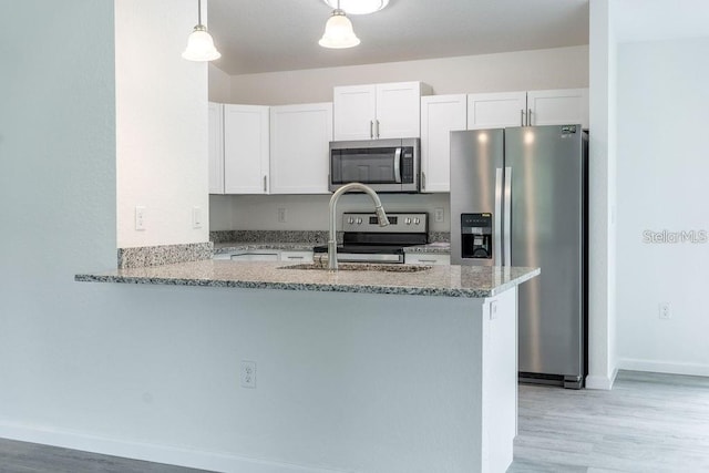 kitchen featuring kitchen peninsula, appliances with stainless steel finishes, light stone countertops, white cabinets, and hanging light fixtures