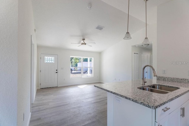 kitchen featuring stone counters, white cabinets, sink, hanging light fixtures, and ceiling fan