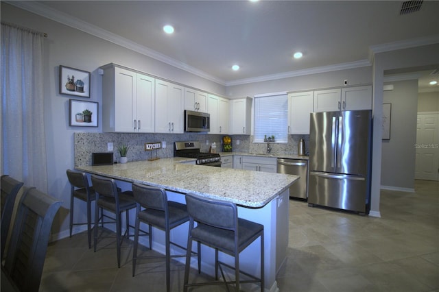 kitchen with kitchen peninsula, a breakfast bar area, light stone counters, white cabinetry, and stainless steel appliances