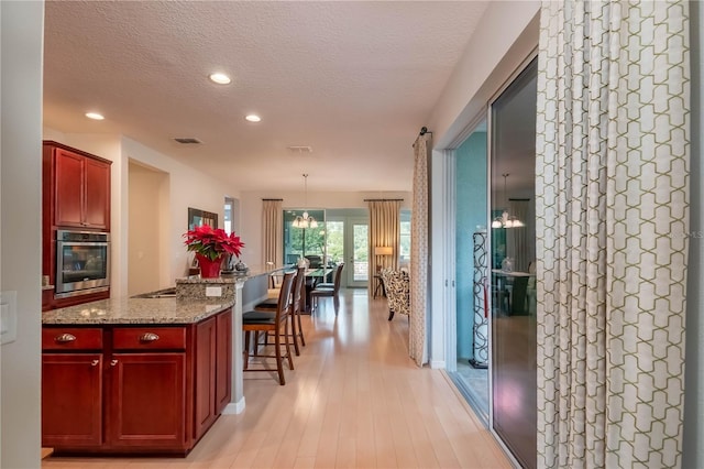 kitchen featuring pendant lighting, oven, light hardwood / wood-style flooring, light stone countertops, and a textured ceiling