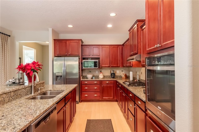 kitchen featuring light stone countertops, sink, appliances with stainless steel finishes, and light hardwood / wood-style flooring