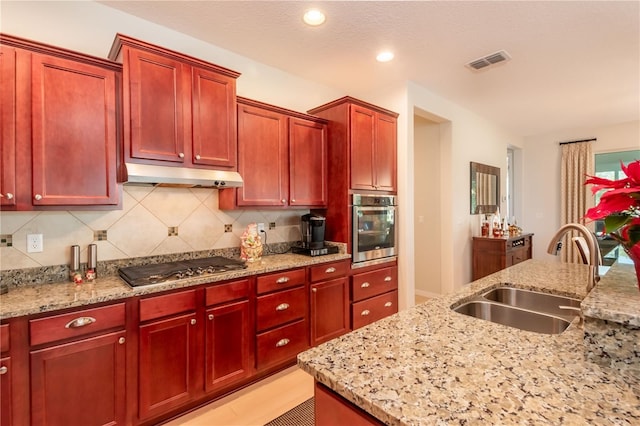 kitchen with light stone counters, stainless steel appliances, sink, and decorative backsplash