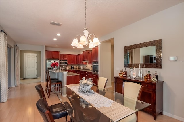 dining space with sink, light hardwood / wood-style floors, and a notable chandelier