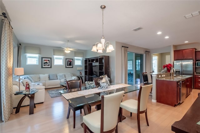 dining space featuring ceiling fan with notable chandelier, sink, and light hardwood / wood-style flooring