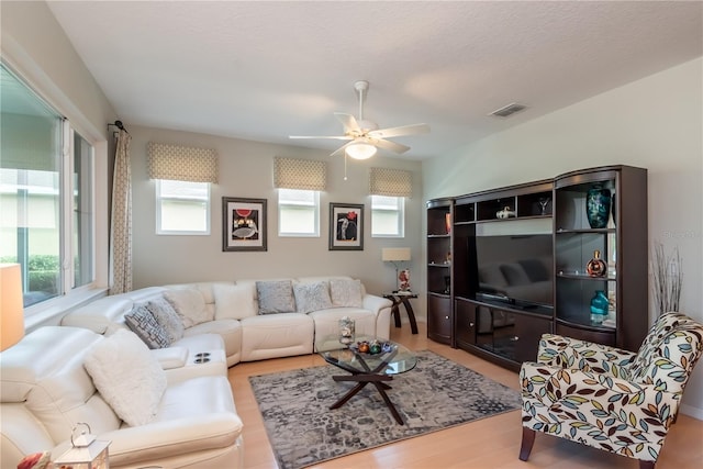 living room with ceiling fan, a textured ceiling, and light wood-type flooring