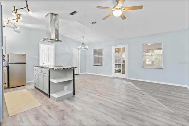 kitchen with island exhaust hood, stainless steel fridge, light stone countertops, decorative light fixtures, and light hardwood / wood-style flooring