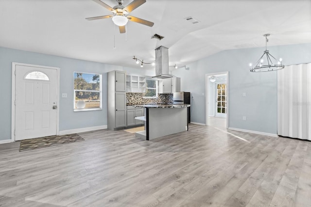 kitchen with tasteful backsplash, island exhaust hood, pendant lighting, gray cabinets, and ceiling fan with notable chandelier