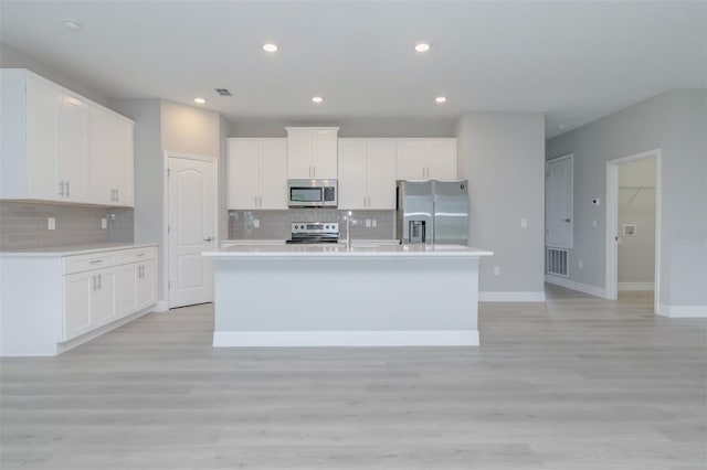 kitchen with a center island with sink, white cabinets, light wood-type flooring, and stainless steel appliances