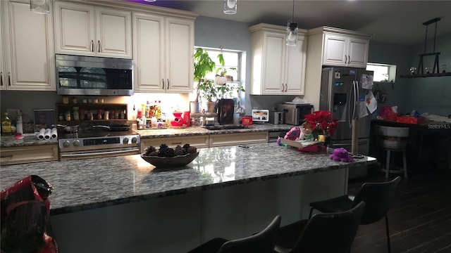 kitchen with light stone countertops, stainless steel appliances, a sink, and decorative light fixtures