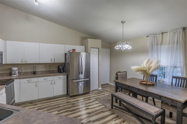 kitchen featuring a notable chandelier, pendant lighting, vaulted ceiling, white cabinets, and appliances with stainless steel finishes