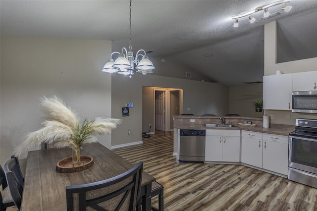 kitchen with lofted ceiling, white cabinetry, a textured ceiling, and appliances with stainless steel finishes