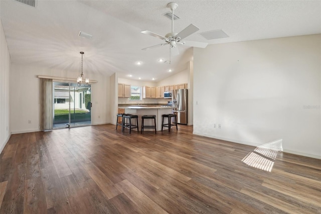 interior space featuring dark wood-type flooring, ceiling fan with notable chandelier, vaulted ceiling, and a textured ceiling