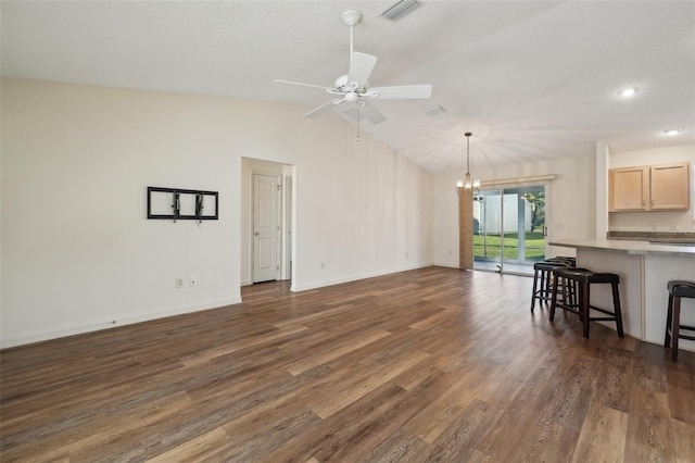 living room with ceiling fan with notable chandelier, dark wood-type flooring, a textured ceiling, and vaulted ceiling