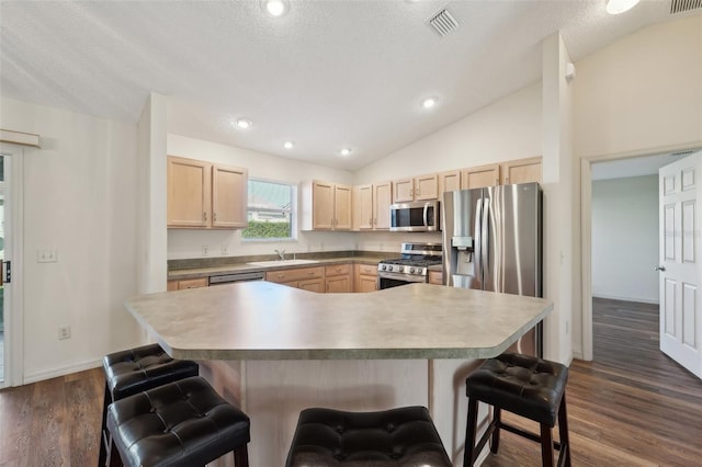 kitchen featuring a kitchen bar, light brown cabinetry, a center island, vaulted ceiling, and stainless steel appliances