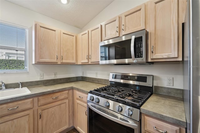 kitchen with sink, vaulted ceiling, a textured ceiling, light brown cabinets, and appliances with stainless steel finishes