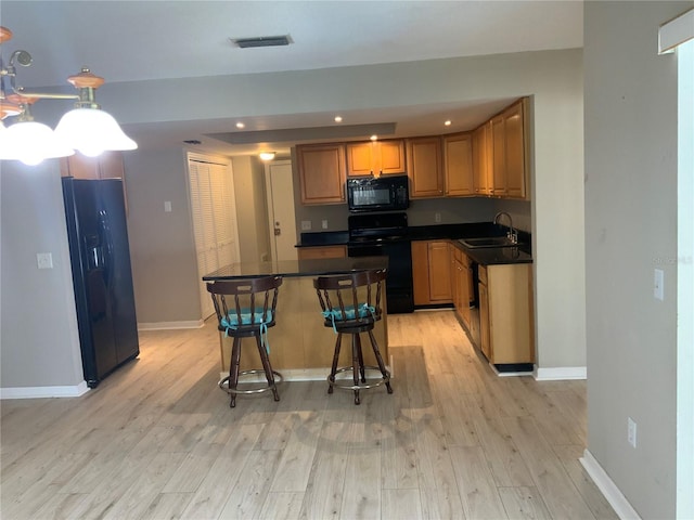 kitchen featuring sink, light hardwood / wood-style flooring, a breakfast bar, a kitchen island, and black appliances