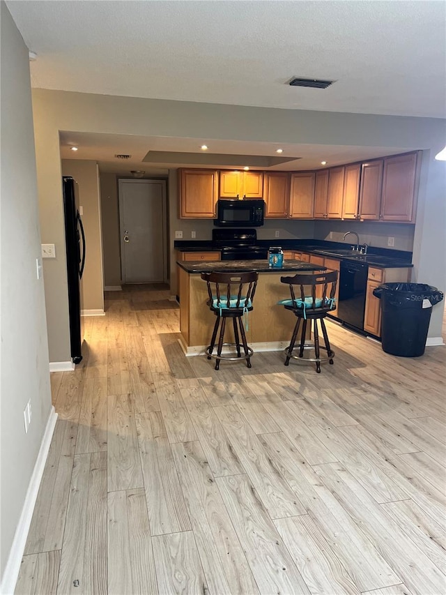 kitchen with sink, black appliances, a center island, light hardwood / wood-style floors, and a breakfast bar area