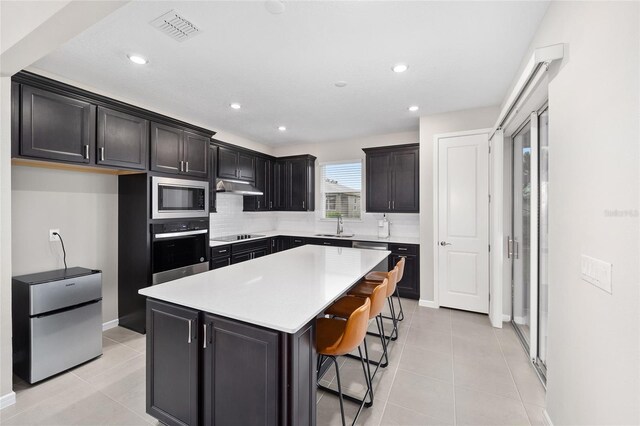 kitchen featuring a center island, light tile patterned floors, stainless steel appliances, and a breakfast bar area