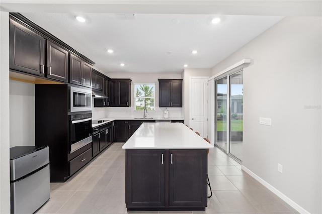 kitchen featuring dark brown cabinets, a kitchen island, light tile patterned flooring, and appliances with stainless steel finishes