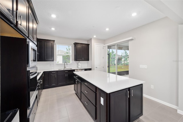 kitchen with appliances with stainless steel finishes, backsplash, sink, a kitchen island, and light tile patterned flooring